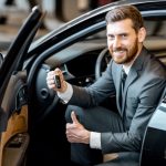Portrait of a handsome businessman holding keys of a luxury car in the showroom